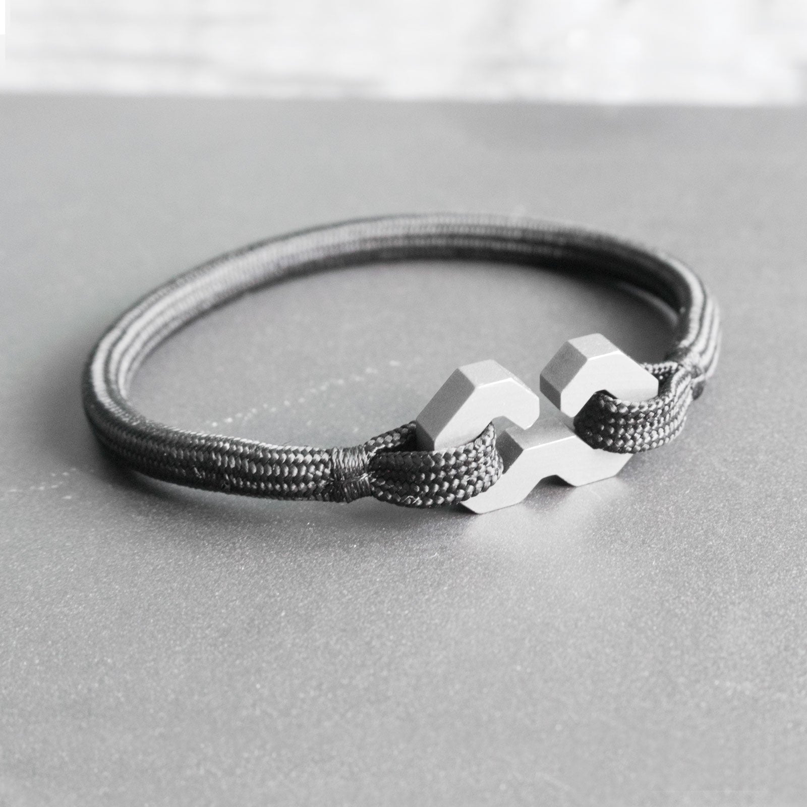 The Menotte is a minimalist and timeless rope bracelet, handmade from grade 5 titanium and a nearly indestructible rope. The clasp is shaped after a shackle or menotte in french. It elegantly ties and holds the rope, making it a very secure and comfortable fit on the wrist.