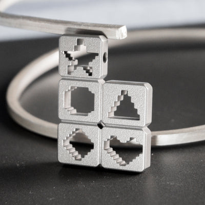 Inspired by the legendary Tetris Attack, several blocks from the game stack next to each other, with their respective symbols precisely cut out from the metal. A minimalist and timeless piece to wear. Entirely handcrafted from grade 5 titanium.