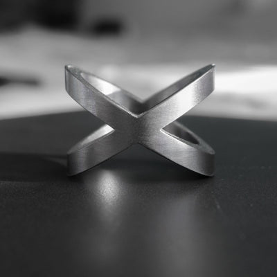 This is the Xenos ring. Shaped after a cross, the massive ring is yet refined, with simple, sharp yet smooth lines. Handcrafted from pure tantalum, the Xenos ring is naturally dark grey, which is the metal's natural color, meaning it will last forever. It also has a bold and weighty presence on the hand, very similar to 18ct gold, and is entirely biocompatible.